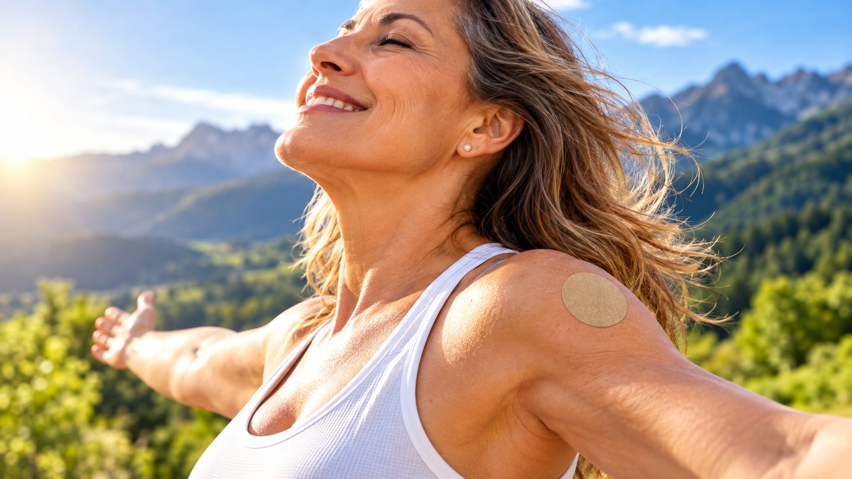 Mujer sonriente con los brazos abiertos frente a un paisaje de montañas, con un parche en el hombro